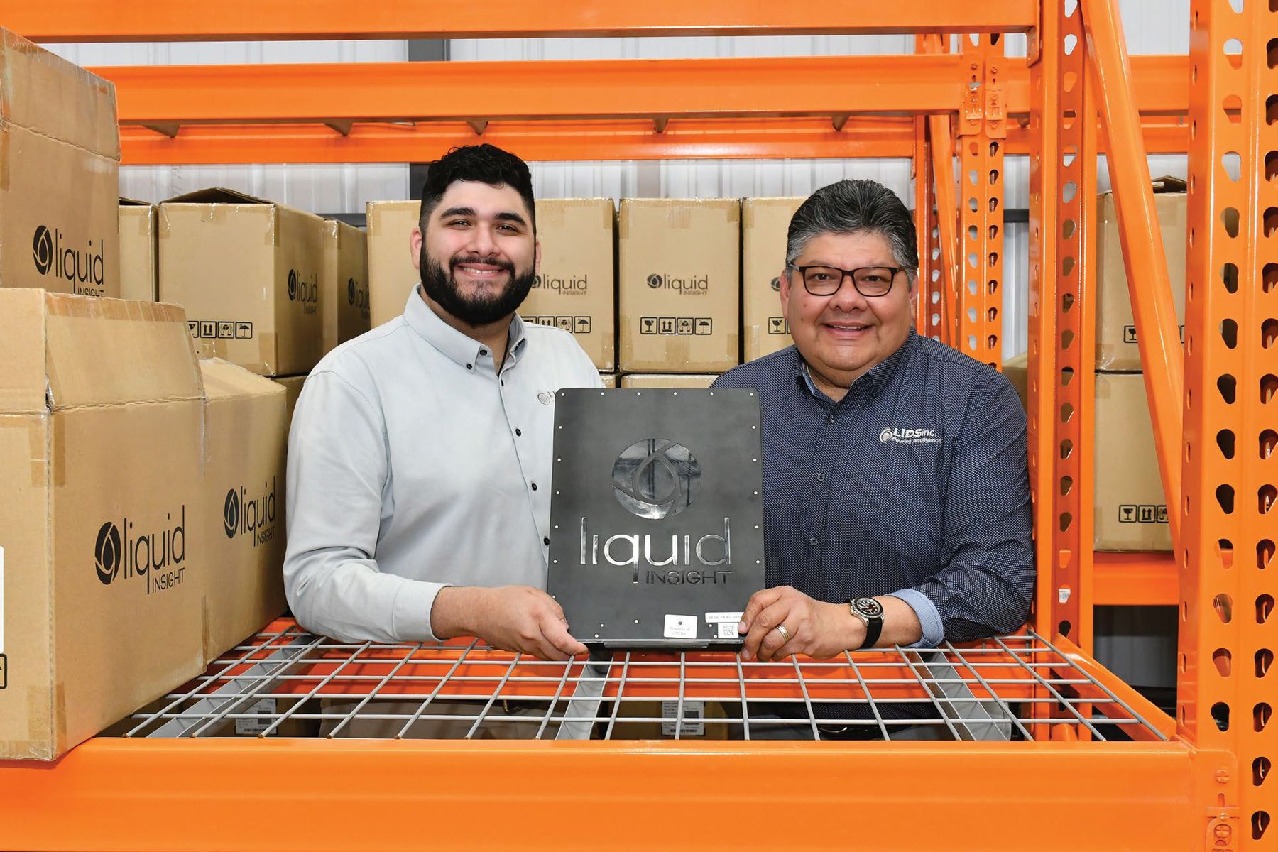 Isaiah and Rudy Ramirez holding a LIDS sensor in front of orange warehouse shelving
